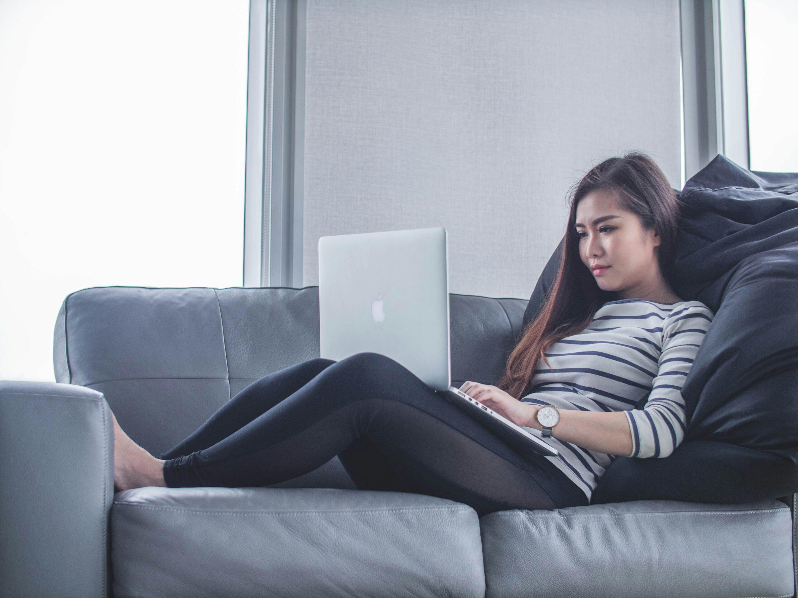 young woman lying on couch with her laptop on her knees