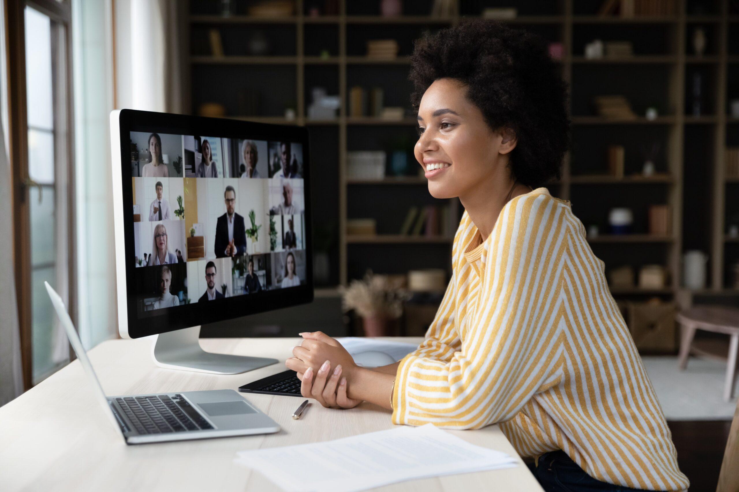 A woman sitting at home facing a computer screen, where there are several faces on the monitor