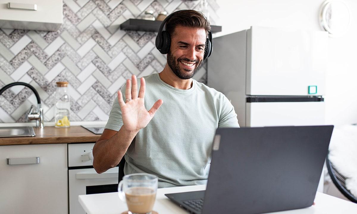 Man on computer working from home, waving to virtual meeting