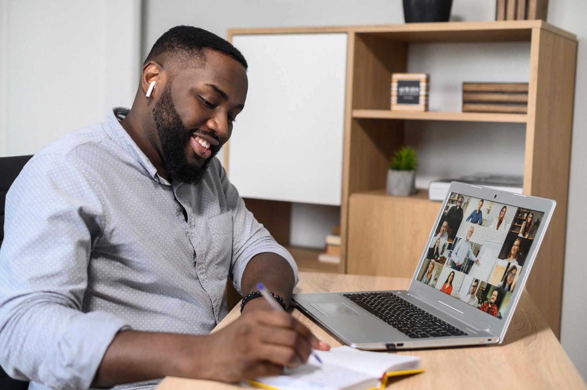 A man takes notes while on a Zoom call on a laptop